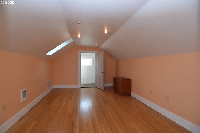 bonus room with lofted ceiling with skylight, light wood-type flooring, visible vents, and baseboards