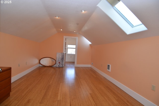 additional living space featuring lofted ceiling with skylight, light wood-type flooring, visible vents, and baseboards