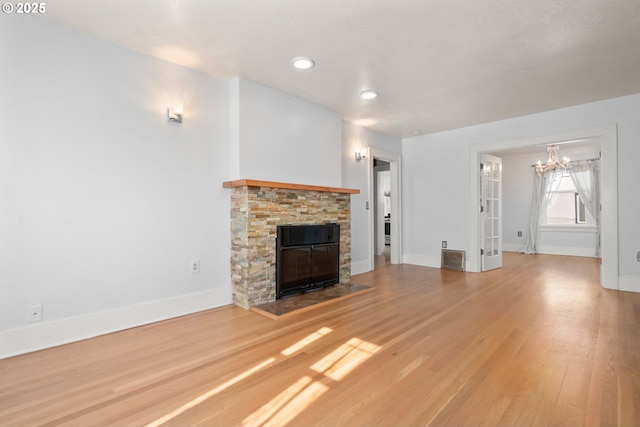 unfurnished living room with a fireplace, visible vents, a chandelier, light wood-type flooring, and baseboards