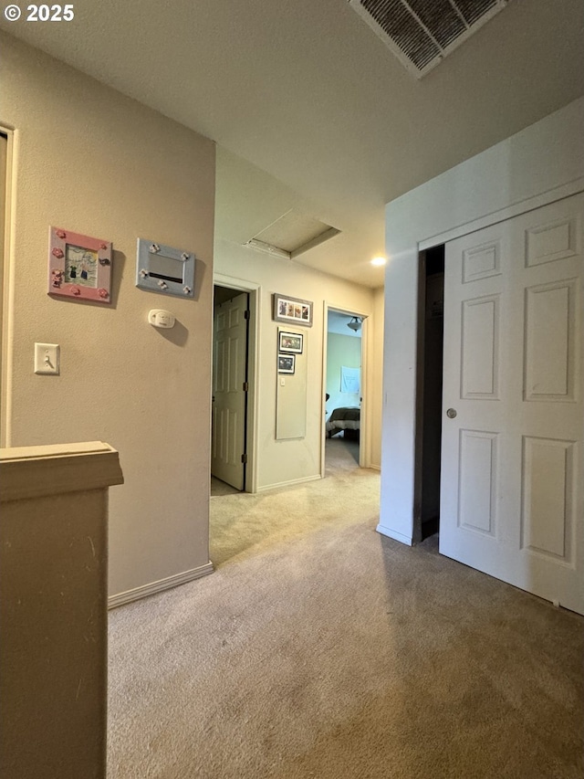 hall with attic access, light carpet, and baseboards
