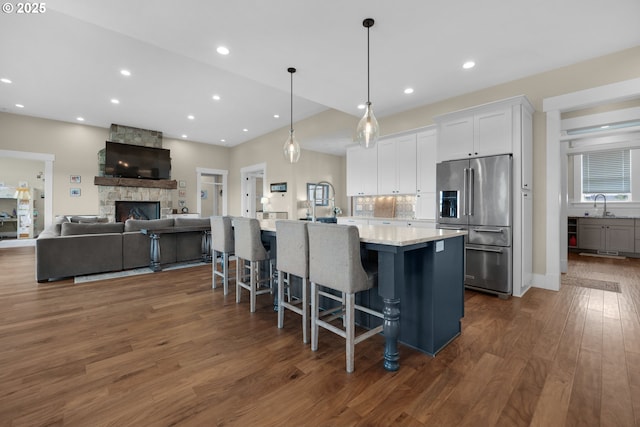 kitchen featuring a breakfast bar, white cabinetry, hanging light fixtures, high quality fridge, and an island with sink