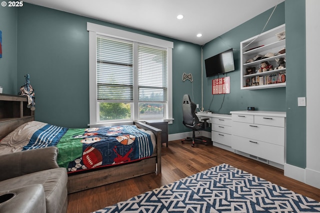 bedroom with built in desk and dark wood-type flooring