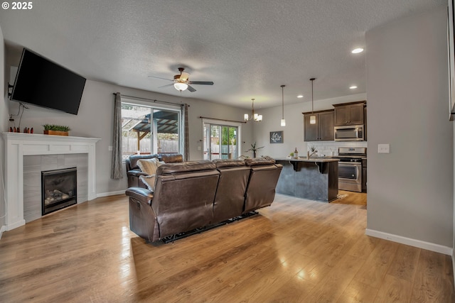 living room featuring a textured ceiling, a tiled fireplace, light hardwood / wood-style flooring, and ceiling fan with notable chandelier