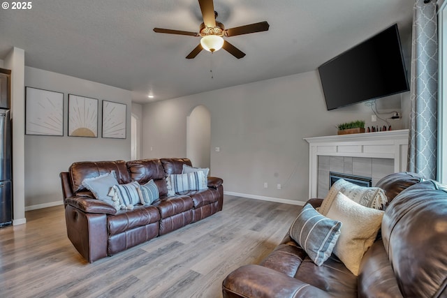 living room featuring ceiling fan, light wood-type flooring, and a tile fireplace