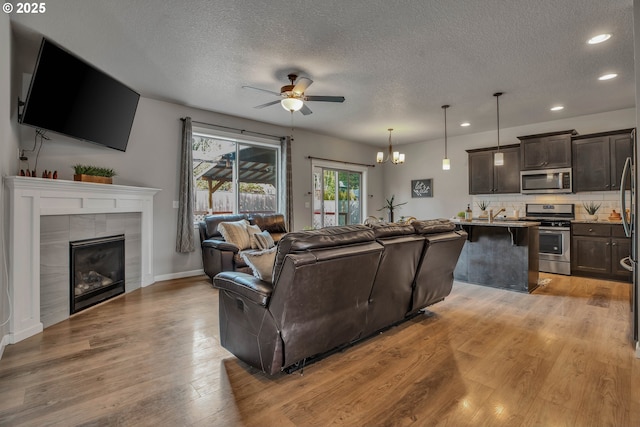 living room with a textured ceiling, a tile fireplace, light hardwood / wood-style floors, and ceiling fan with notable chandelier