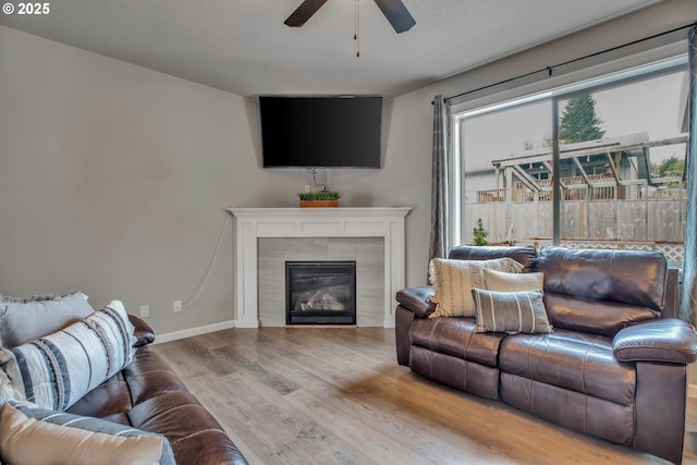 living room with a textured ceiling, light wood-type flooring, ceiling fan, and a tiled fireplace