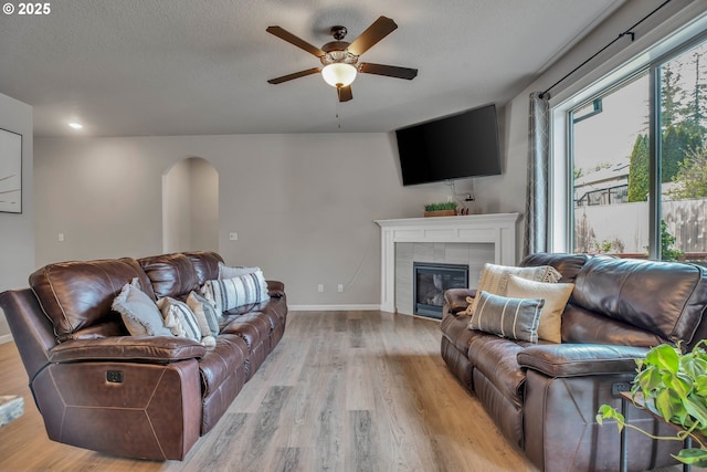 living room featuring a textured ceiling, light wood-type flooring, ceiling fan, and a tiled fireplace