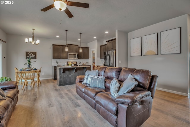 living room featuring ceiling fan with notable chandelier, a textured ceiling, and light hardwood / wood-style flooring