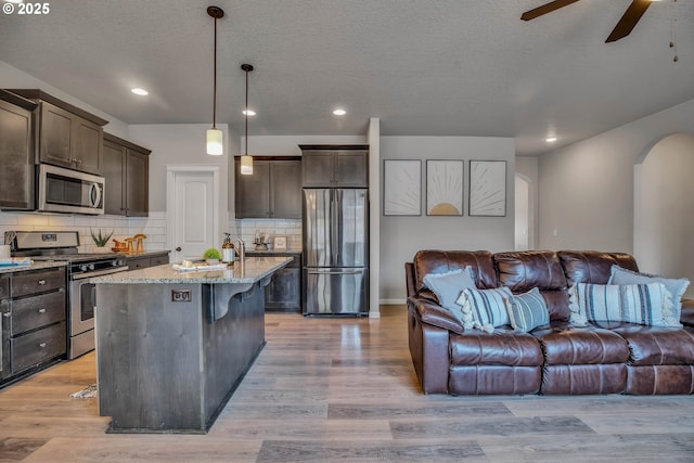 kitchen featuring light hardwood / wood-style flooring, an island with sink, decorative light fixtures, and appliances with stainless steel finishes