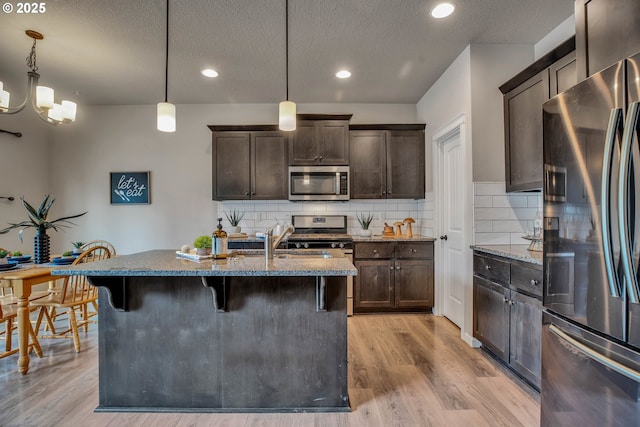 kitchen with light hardwood / wood-style flooring, appliances with stainless steel finishes, decorative light fixtures, light stone counters, and dark brown cabinetry