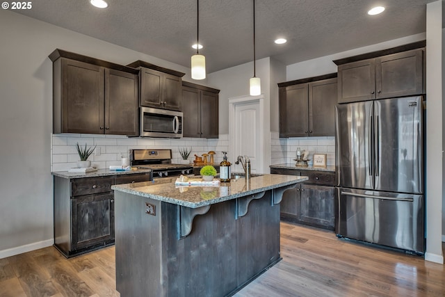 kitchen with light wood-type flooring, a textured ceiling, light stone countertops, decorative light fixtures, and stainless steel appliances