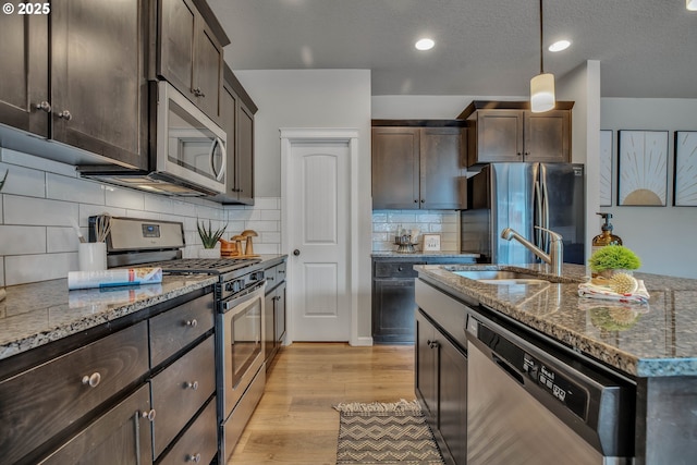 kitchen with pendant lighting, stone counters, appliances with stainless steel finishes, and light hardwood / wood-style flooring