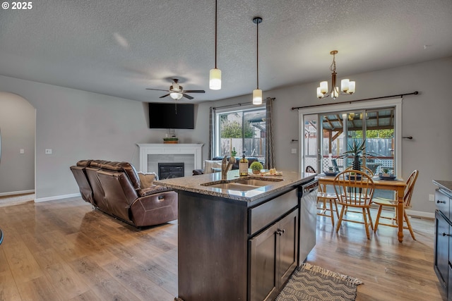 kitchen with a kitchen island with sink, ceiling fan with notable chandelier, hanging light fixtures, a fireplace, and dark brown cabinetry