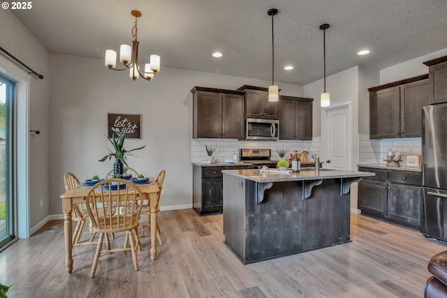 kitchen with pendant lighting, light stone counters, a center island with sink, and stainless steel appliances