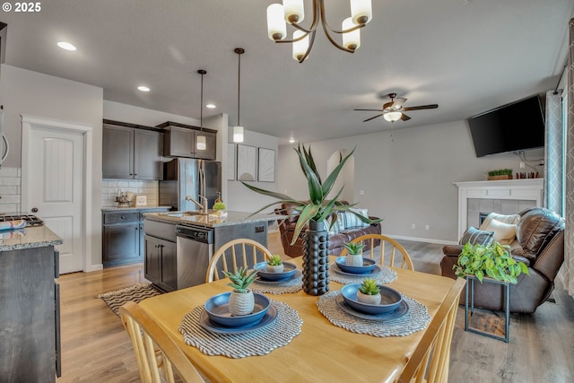 dining space featuring ceiling fan with notable chandelier, light hardwood / wood-style floors, sink, and a tile fireplace