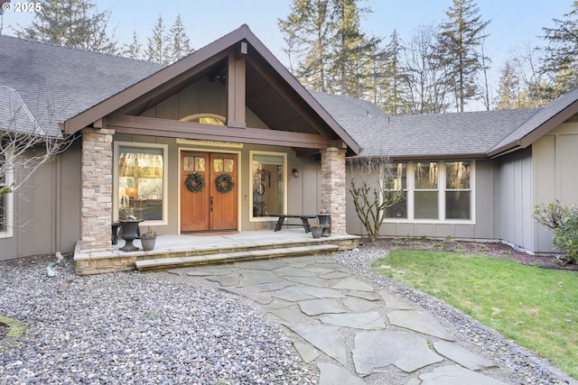 entrance to property featuring a shingled roof, covered porch, stone siding, and board and batten siding