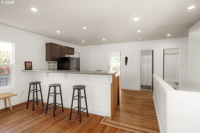 kitchen featuring recessed lighting, freestanding refrigerator, baseboards, light wood-type flooring, and a kitchen breakfast bar