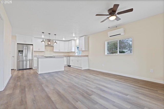 kitchen featuring pendant lighting, light countertops, a wall mounted AC, appliances with stainless steel finishes, and white cabinetry