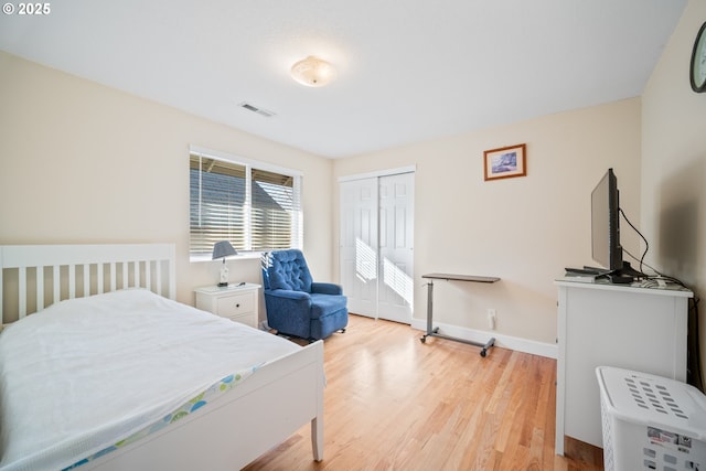 bedroom with wood finished floors, visible vents, a closet, and baseboards