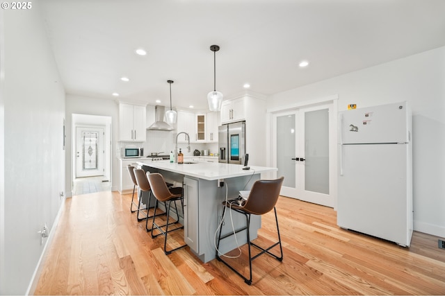 kitchen featuring wall chimney range hood, freestanding refrigerator, light wood-style floors, stainless steel refrigerator with ice dispenser, and white cabinetry