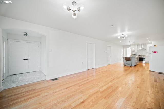 unfurnished living room featuring visible vents, baseboards, arched walkways, a sink, and light wood-style floors