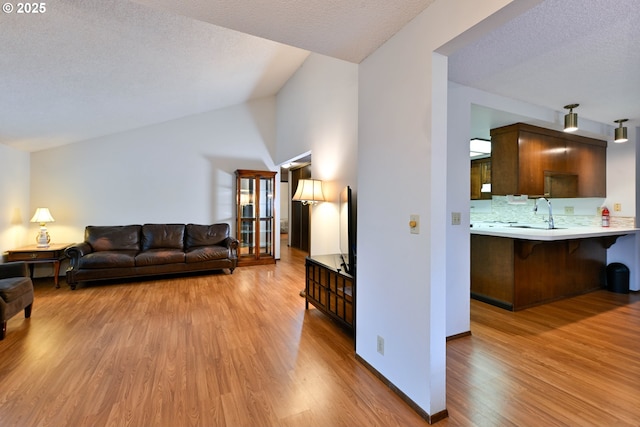 living room featuring light wood-type flooring, vaulted ceiling, a textured ceiling, and baseboards