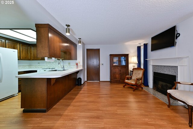 kitchen with freestanding refrigerator, a sink, light countertops, a textured ceiling, and light wood-style flooring