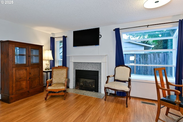 living area featuring a textured ceiling, light wood-style flooring, and a fireplace with flush hearth