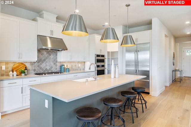 kitchen with a kitchen island with sink, white cabinetry, stainless steel appliances, and decorative light fixtures