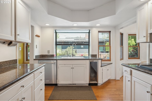 kitchen featuring a sink, dishwasher, beverage cooler, light wood-style flooring, and white cabinetry