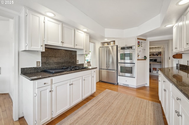 kitchen featuring backsplash, dark stone countertops, light wood finished floors, stainless steel appliances, and white cabinetry