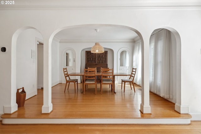 dining space featuring arched walkways, ornamental molding, baseboards, and wood finished floors