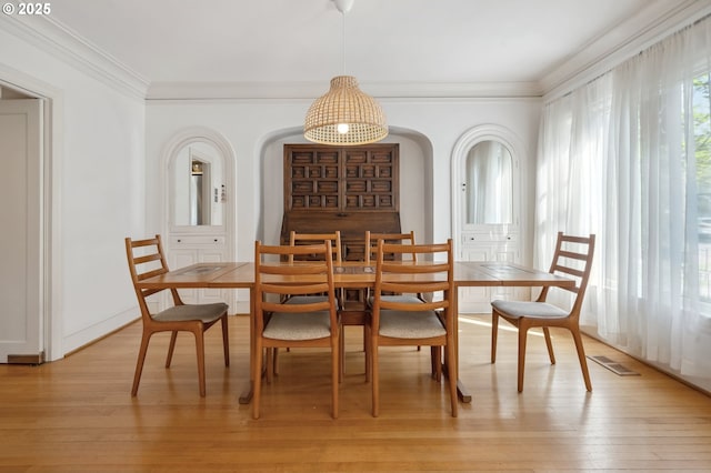 dining room with crown molding, arched walkways, visible vents, and light wood finished floors
