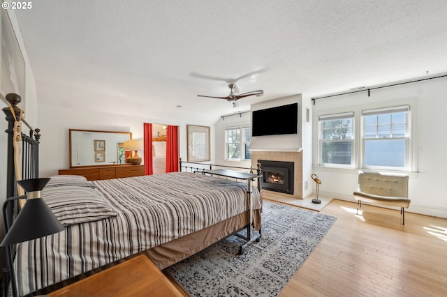 bedroom featuring baseboards, wood-type flooring, a textured ceiling, and a tile fireplace