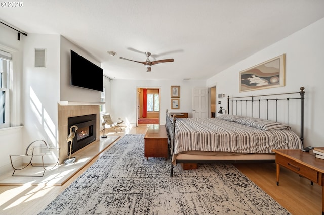 bedroom featuring a tiled fireplace, a ceiling fan, wood finished floors, and visible vents