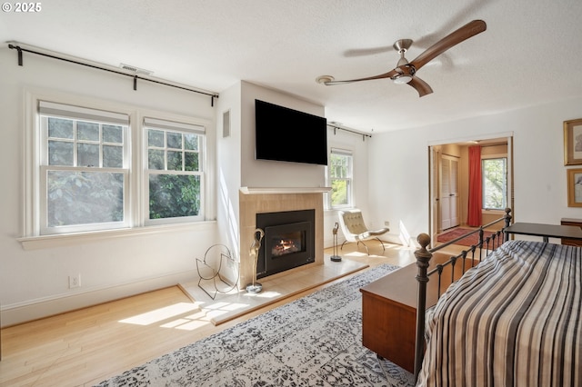 bedroom featuring a textured ceiling, baseboards, wood finished floors, a tile fireplace, and visible vents