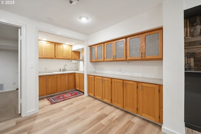 kitchen with light wood-style floors, light countertops, a sink, and brown cabinetry