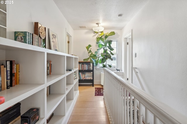 hall featuring a textured ceiling, visible vents, and light wood finished floors