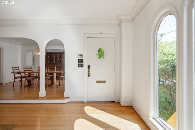 entrance foyer featuring ornamental molding, light wood-style flooring, and arched walkways