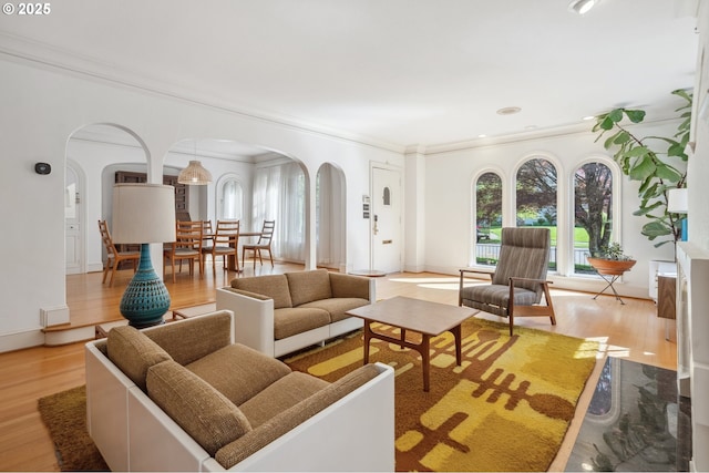 living area featuring crown molding, arched walkways, light wood-style flooring, and baseboards