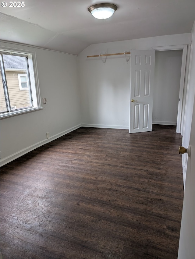 empty room with lofted ceiling, dark wood finished floors, and baseboards
