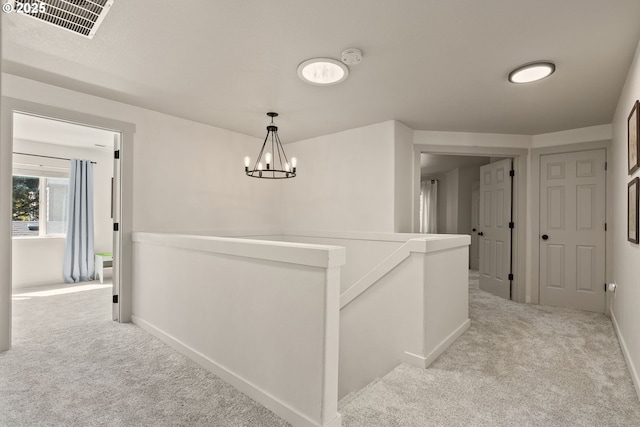 corridor with carpet floors, baseboards, a chandelier, and an upstairs landing