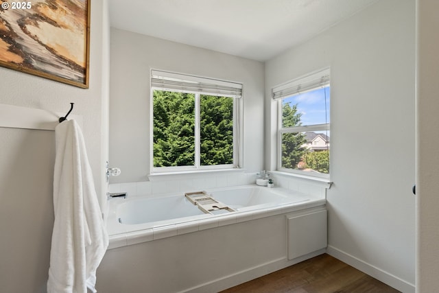 bathroom with a bath, baseboards, and wood finished floors