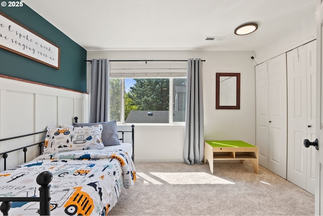 bedroom with visible vents, wainscoting, carpet, and a closet