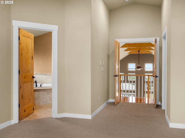 corridor featuring baseboards, high vaulted ceiling, and light colored carpet