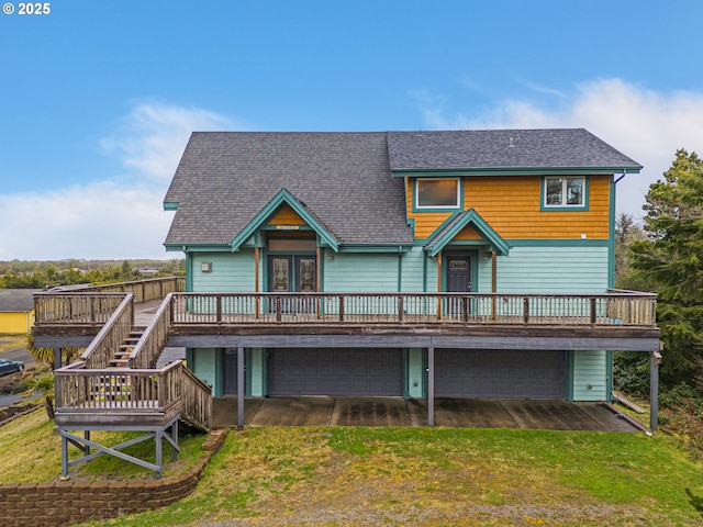 rear view of house featuring roof with shingles, a lawn, a garage, driveway, and a wooden deck