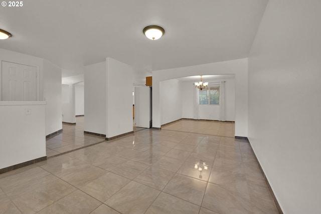 empty room with baseboards, a chandelier, and light tile patterned floors