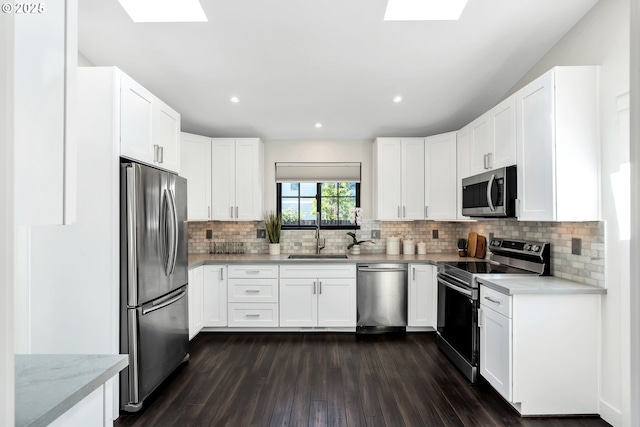 kitchen featuring appliances with stainless steel finishes, a skylight, a sink, dark wood-style floors, and recessed lighting