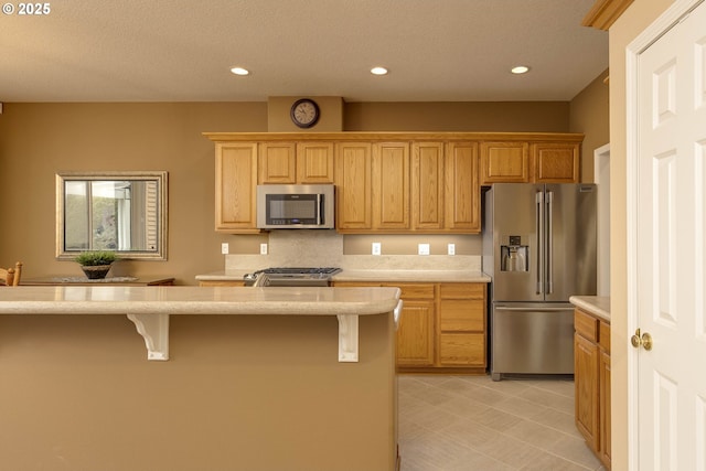 kitchen with a kitchen bar, stainless steel appliances, a textured ceiling, and recessed lighting