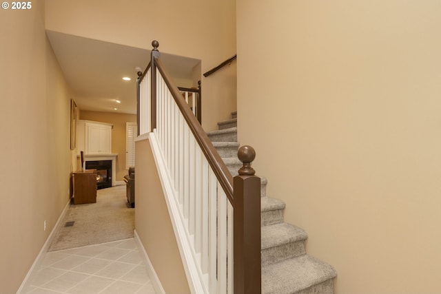 stairway featuring carpet floors, recessed lighting, a glass covered fireplace, baseboards, and tile patterned floors